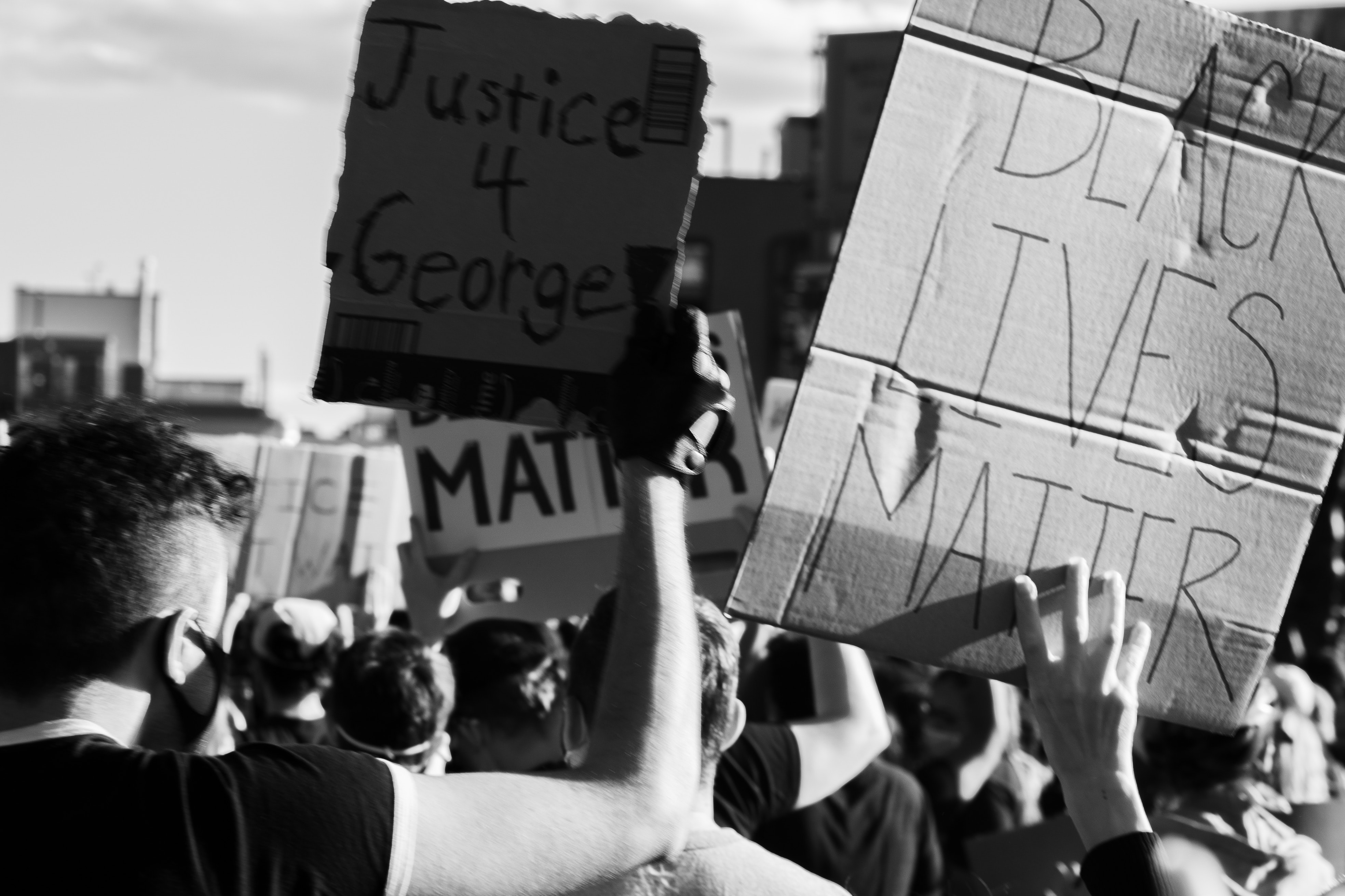 A black and white photo of a crowd of protestors holding up signs like 'Justice 4 George' and 'Black Lives Matter'.